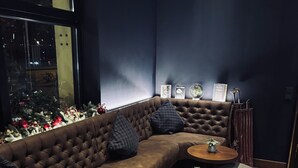 A modern lounge area with a brown leather sofa, multiple round wooden tables, and grey ottomans. - Hotel Allegro (Cologne)