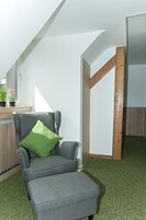 Una habitación moderna con un sillón gris, un cojín verde y estructura de vigas de madera.