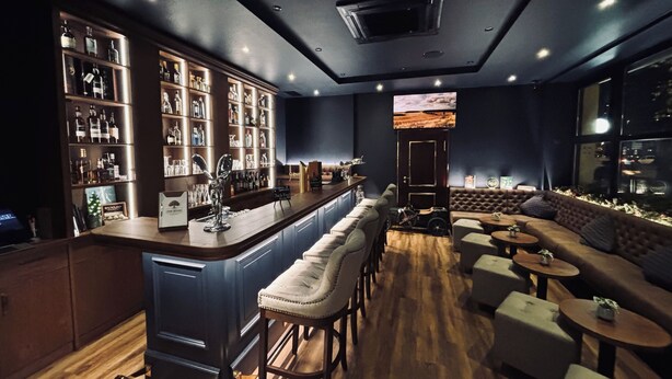 A bar area with a long counter, stools, and a seating area with sofas and round tables. - Hotel Allegro (Cologne)