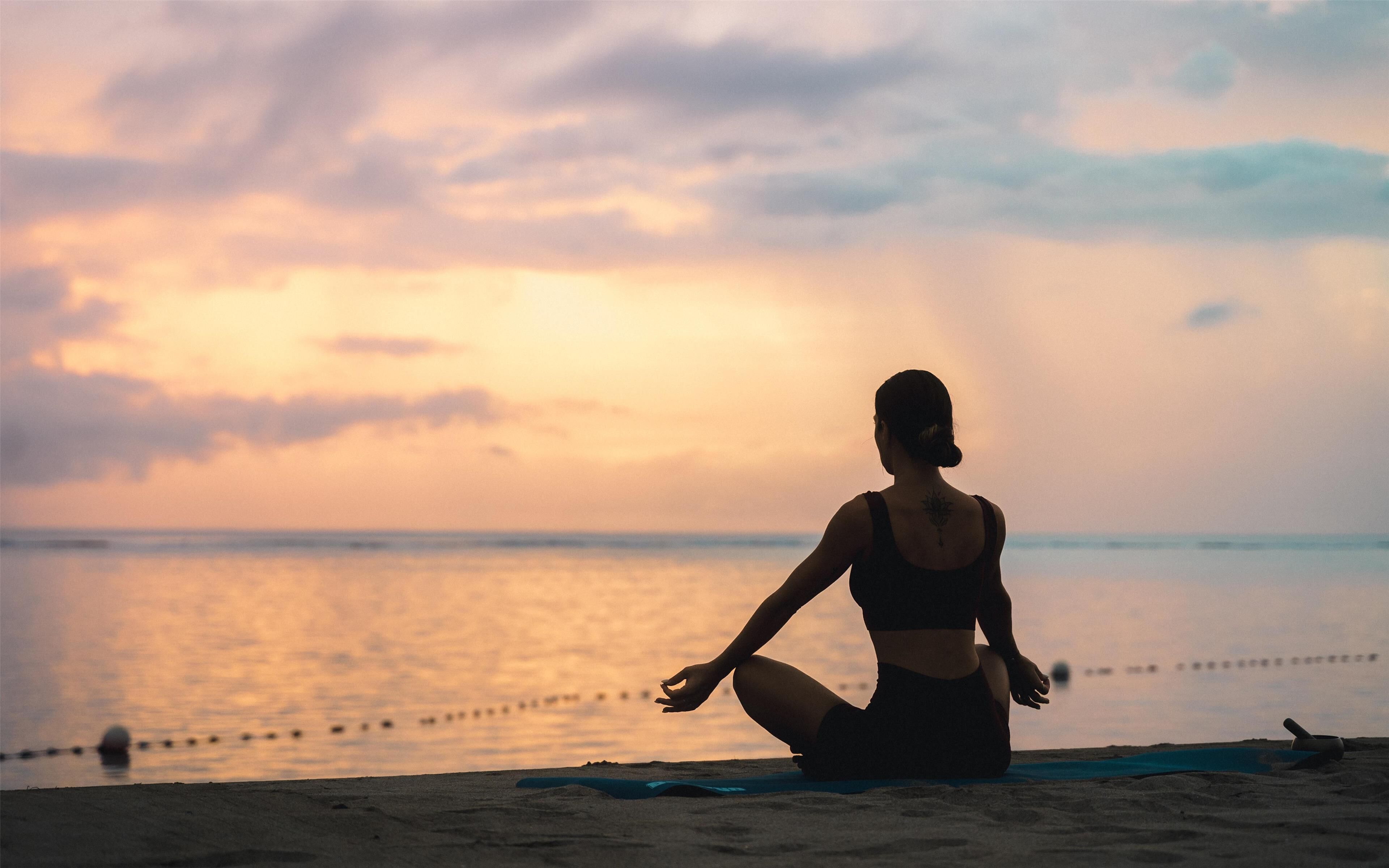 A person sitting on a beach towel, facing the ocean at sunset.