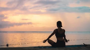 A person sitting on a beach towel, facing the ocean at sunset.