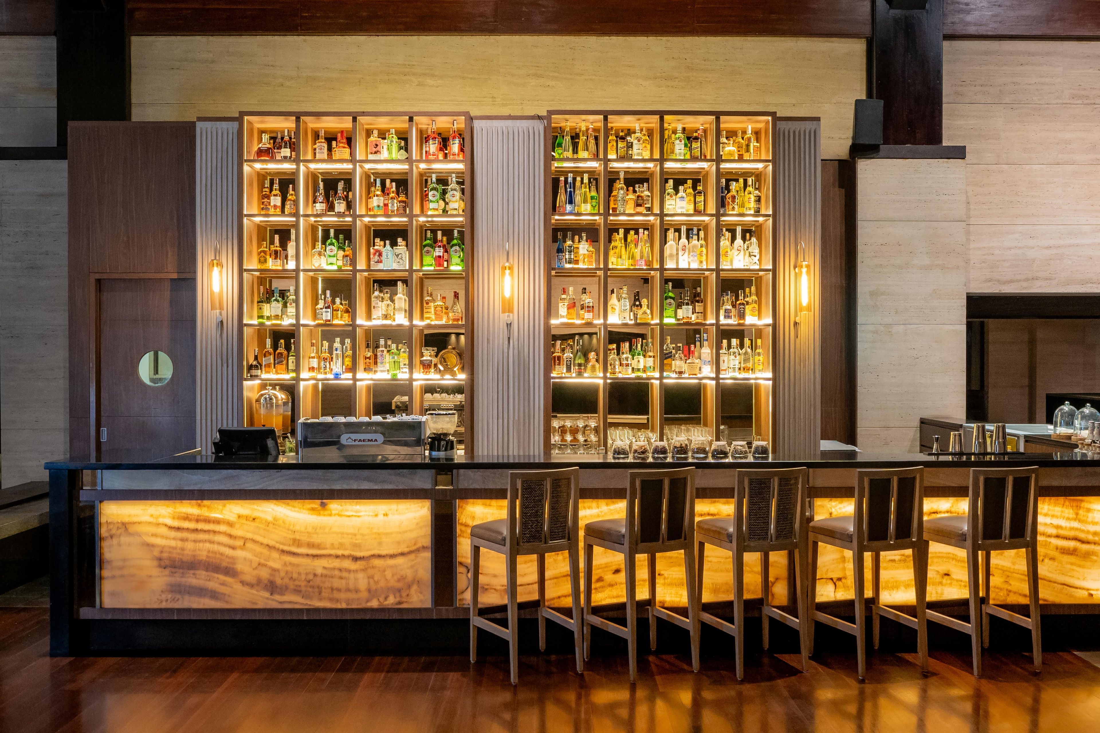 A bar area with multiple shelves of liquor bottles, a cash register, and bar stools.