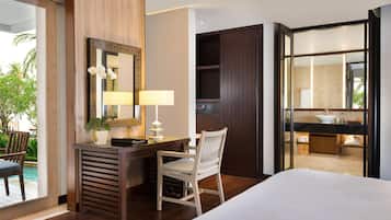 Quarto de hotel com cama, escrivaninha com luminária, cadeira, espelho grande e vista para a piscina e área externa.