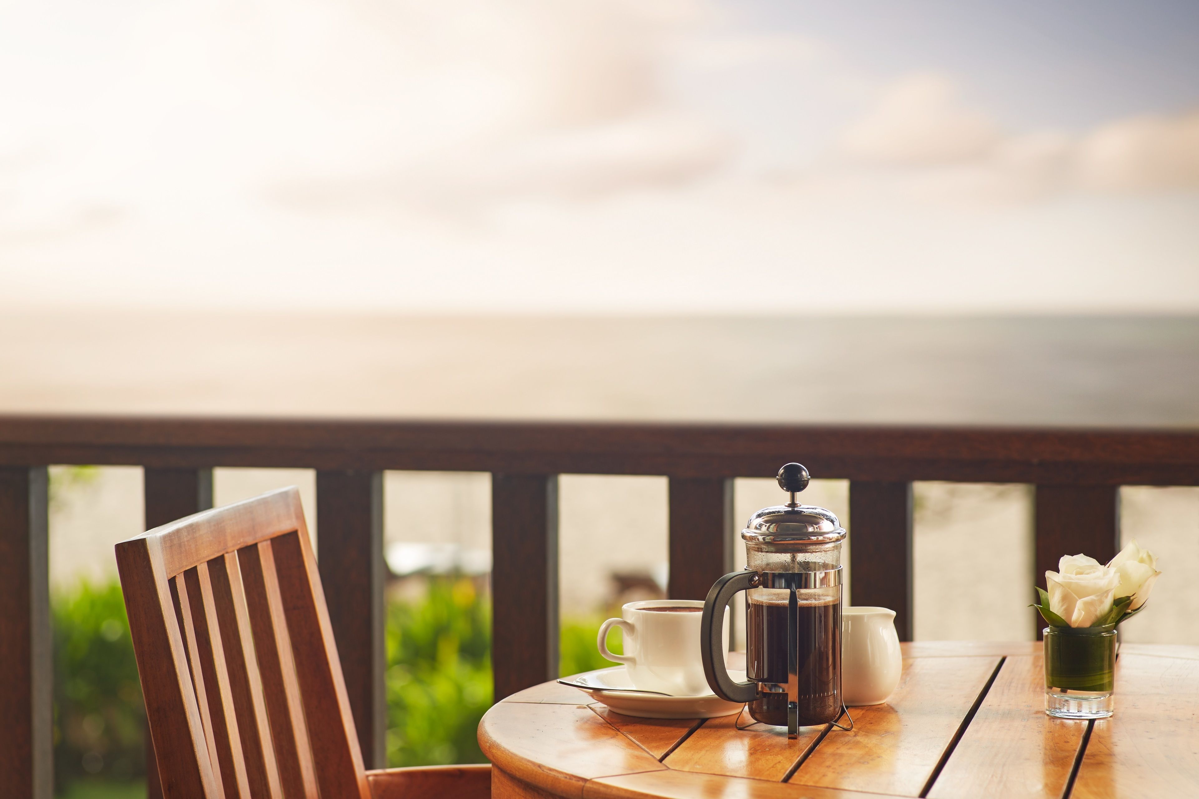 A wooden table with a coffee maker, a cup, and a vase with flowers.
