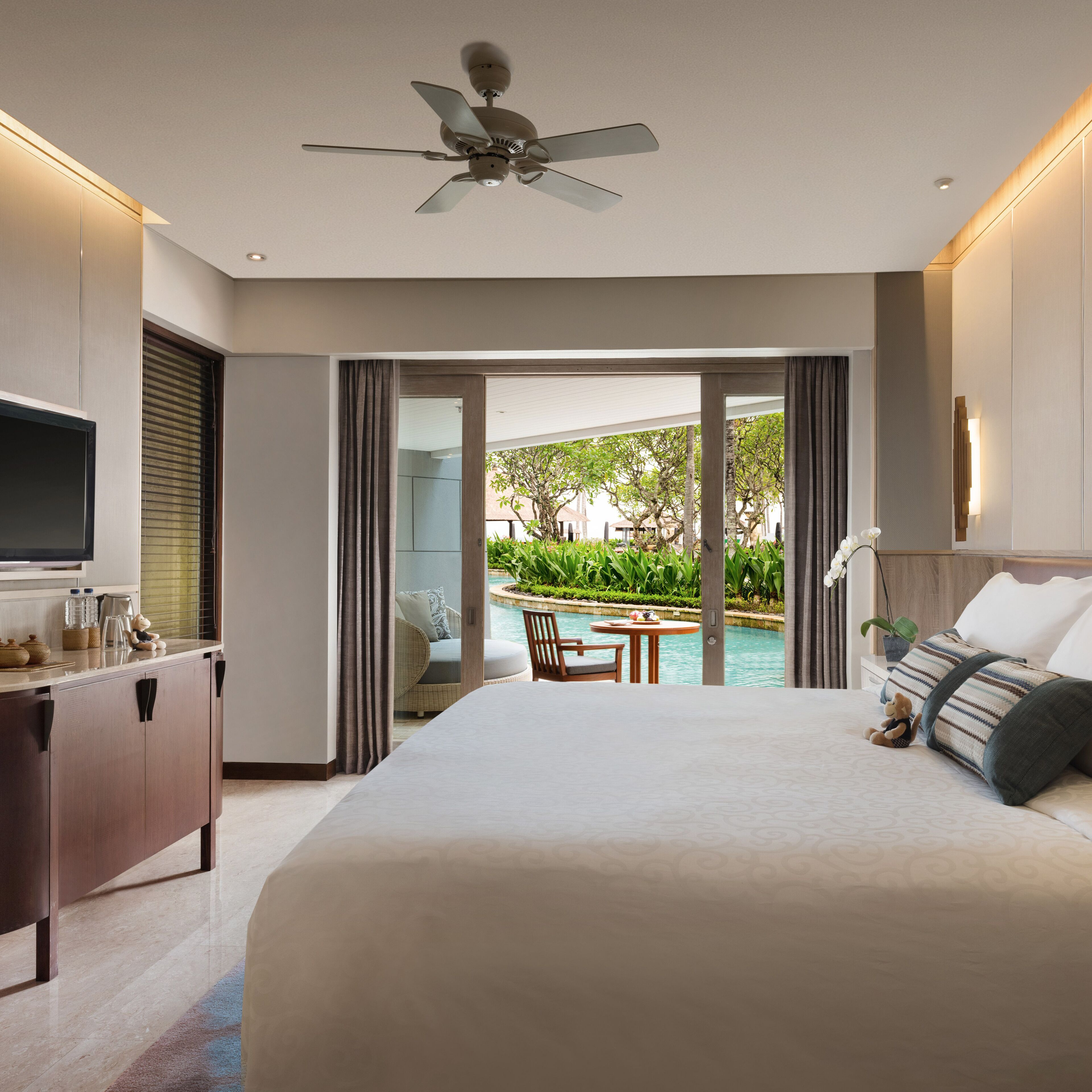 Un dormitorio de hotel moderno con una cama grande, un escritorio y vistas a una piscina y jardín.