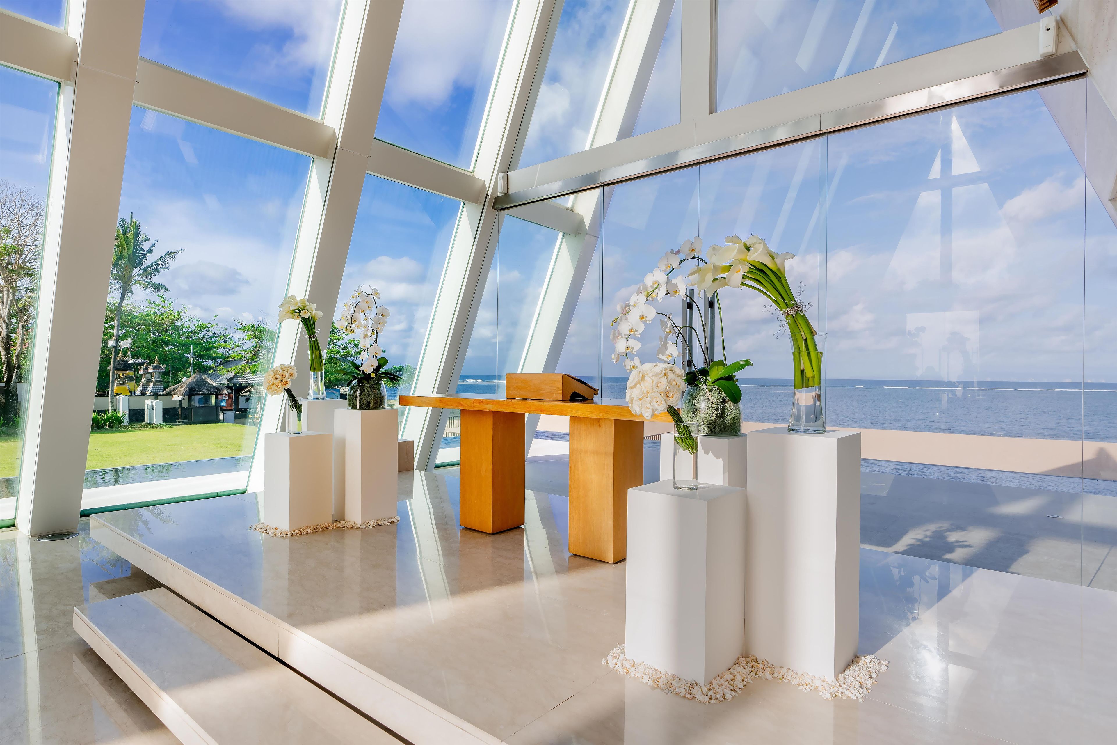 Un interior moderno con un separador de vidrio, una mesa de madera y arreglos florales blancos.