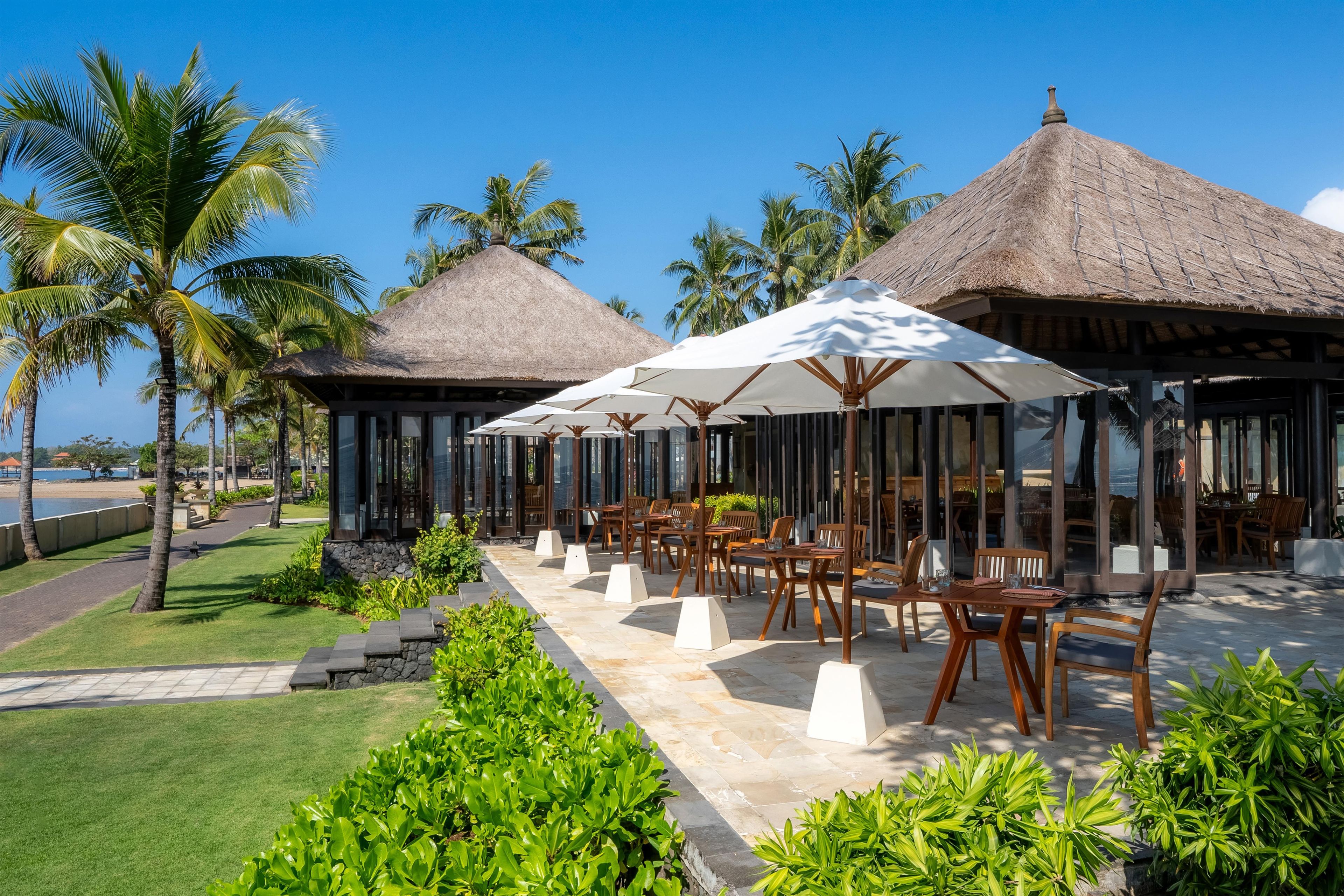 A resort with thatched-roof structures, outdoor seating, and palm trees.