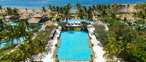 A resort with a central pool, palm trees, and a beach view.