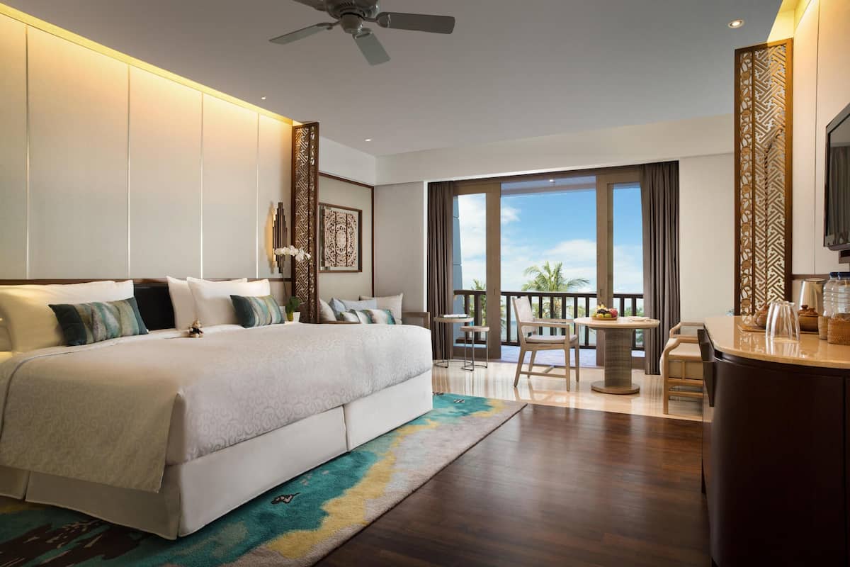 Una habitación de hotel moderna con una cama grande, un balcón con vistas, un escritorio y un ventilador de techo.