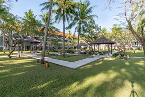 A resort courtyard with palm trees, thatched-roof gazebos, and a well-maintained lawn.