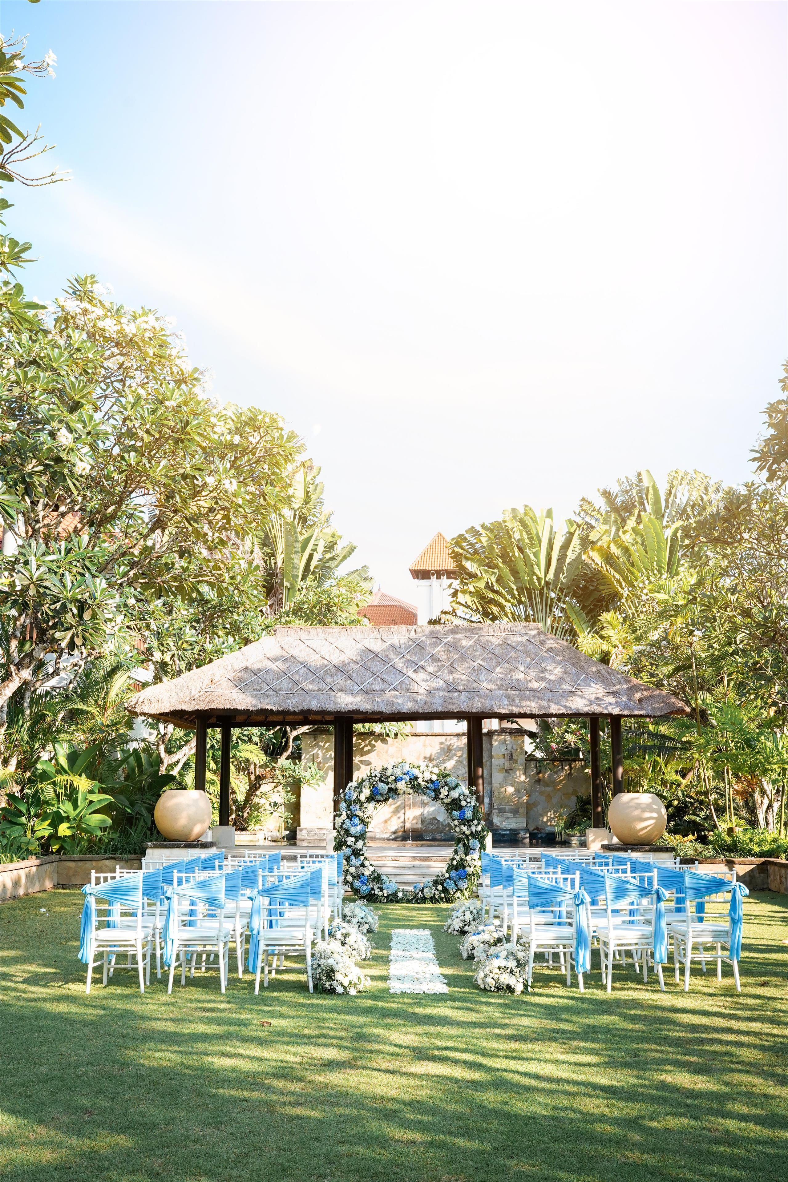 An outdoor wedding ceremony setup with a gazebo, white chairs, and floral decorations.