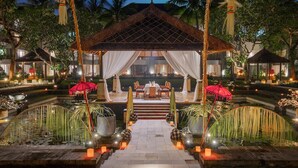 A nighttime view of a resort with a central pavilion, palm trees, and a moon in the sky. - Conrad Bali (Nusa Dua)