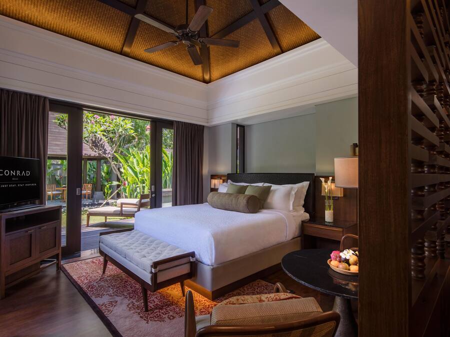 A spacious bedroom with a large bed, a television, and a dining area with a fruit bowl.