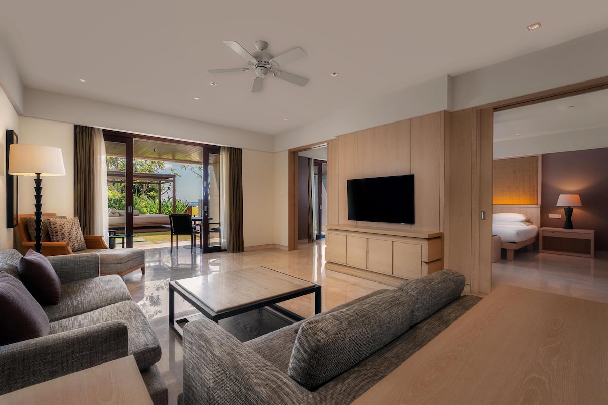 Habitación de hotel moderna con televisor de pantalla plana, ventilador de techo, sofá, mesa de centro y vistas al exterior.