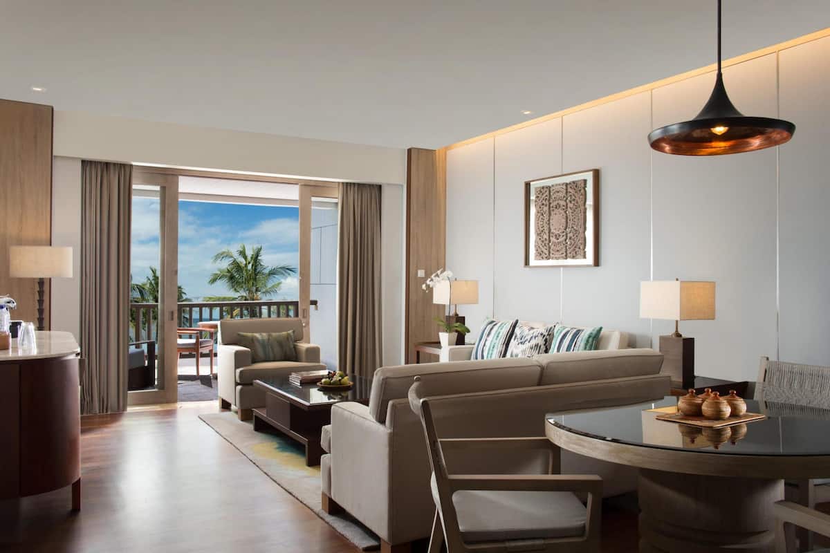 Una habitación de hotel moderna con un balcón grande, una mesa de comedor redonda y un conjunto de sofás.