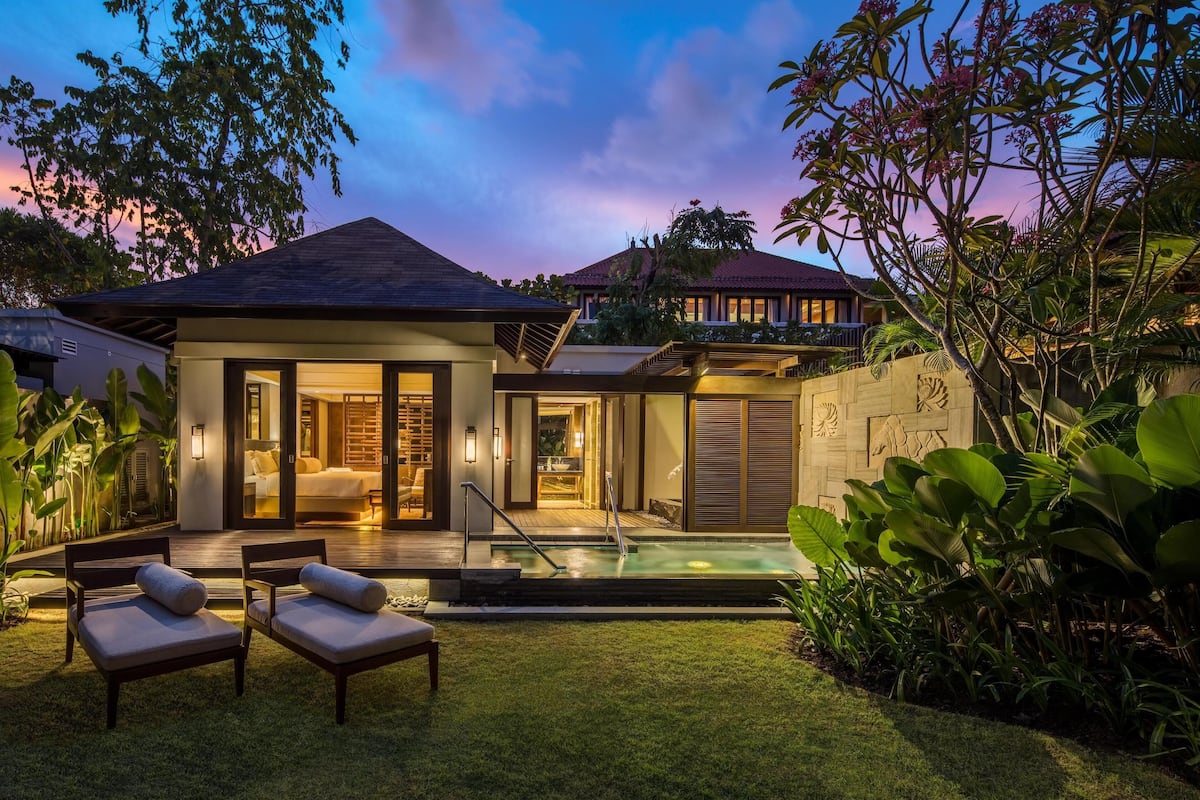 Una villa moderna con piscina, mobiliario exterior y exuberante jardinería tropical.
