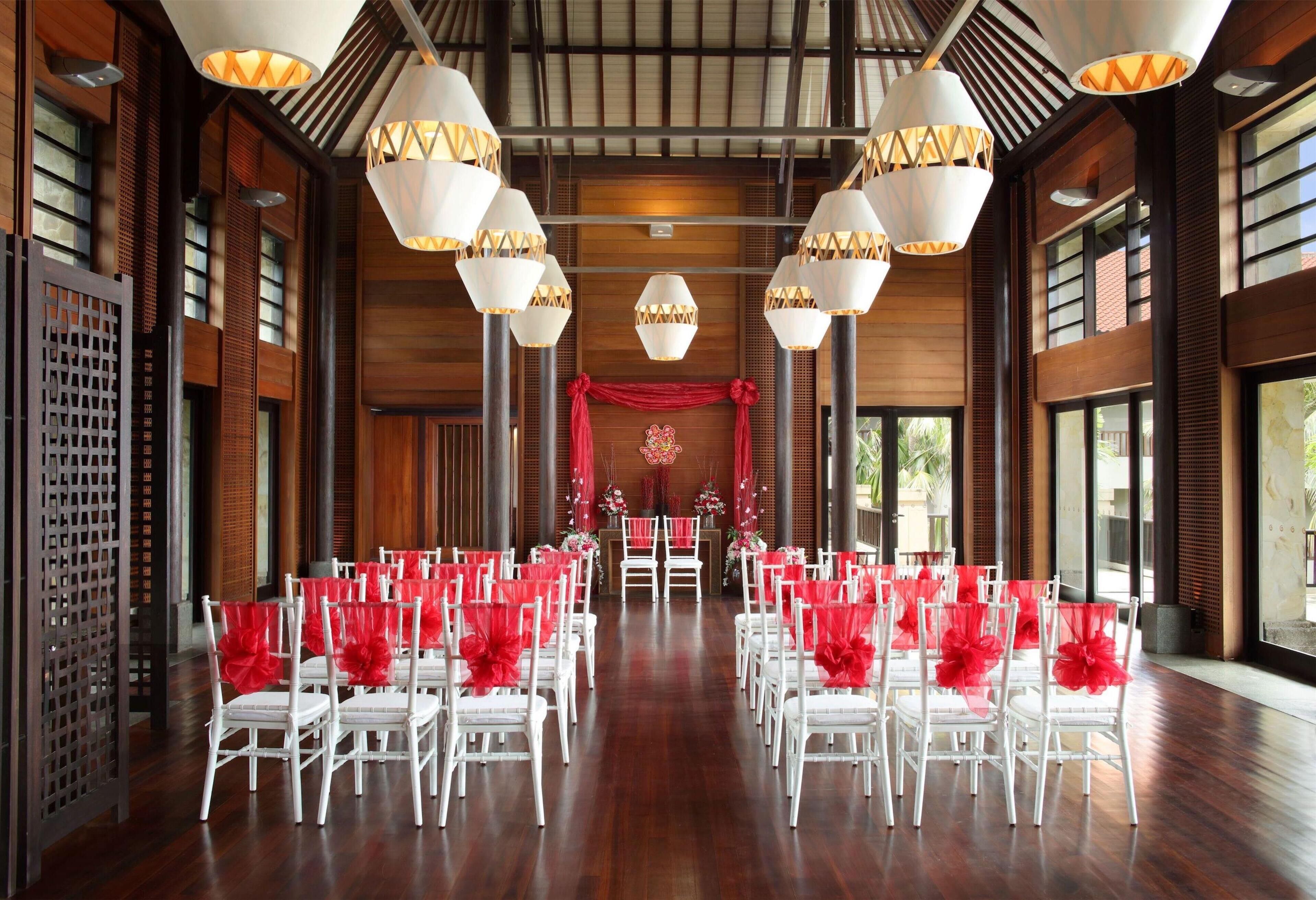 A spacious hall with rows of white chairs, red chair covers, and decorative lighting fixtures.
