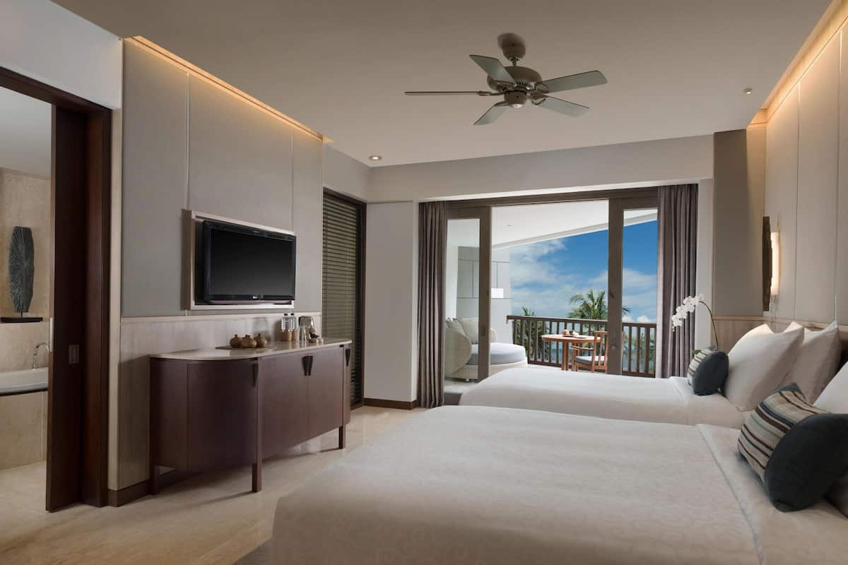 Una habitación de hotel moderna con una cama grande, un televisor, un balcón con vistas y un ventilador de techo.