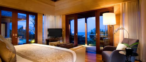 A spacious bedroom with a large bed, a television, and a seating area by a large window with a view of the outdoors.