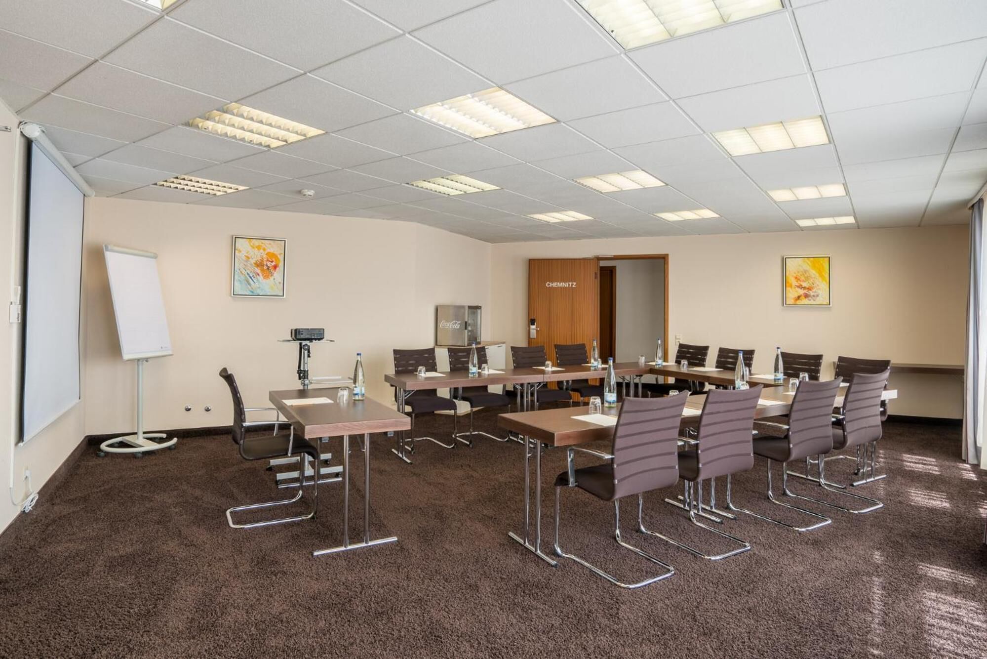 A conference room with a whiteboard, projector, and Coca-Cola refrigerator.