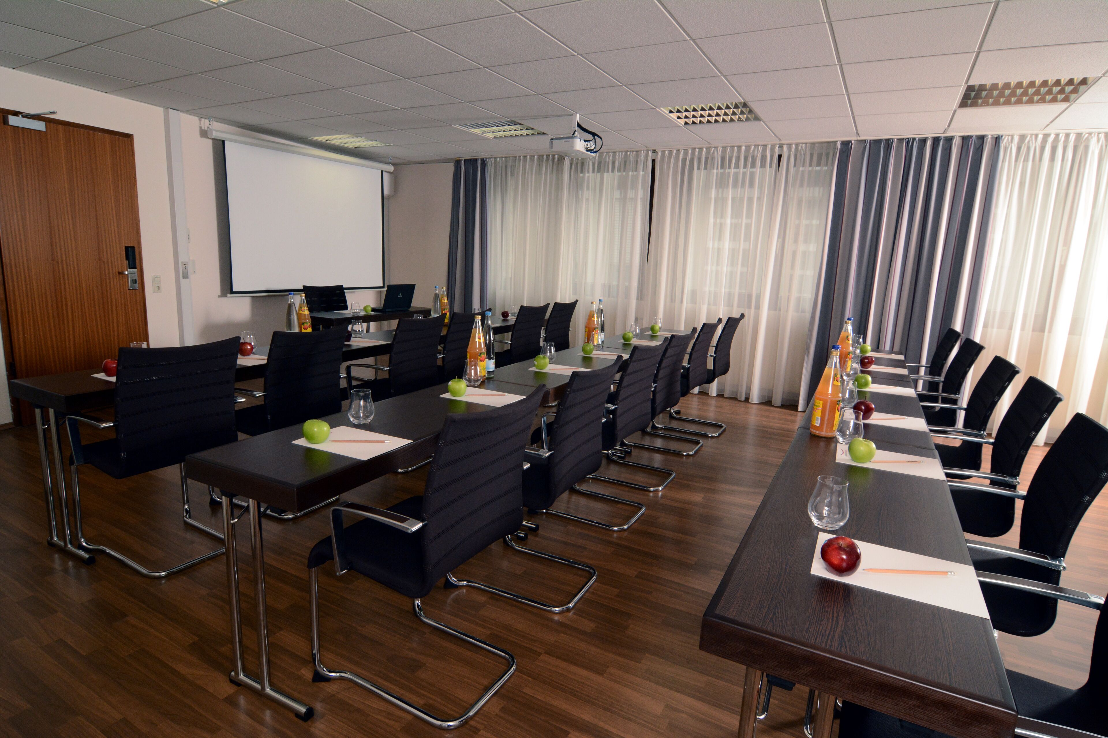 A conference room with a long table, chairs, a projector screen, and a whiteboard.
