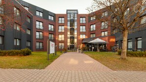 Un bâtiment moderne doté d’un atrium central, d’un espace extérieur aménagé pour s’asseoir et d’un chemin pavé menant à l’entrée.