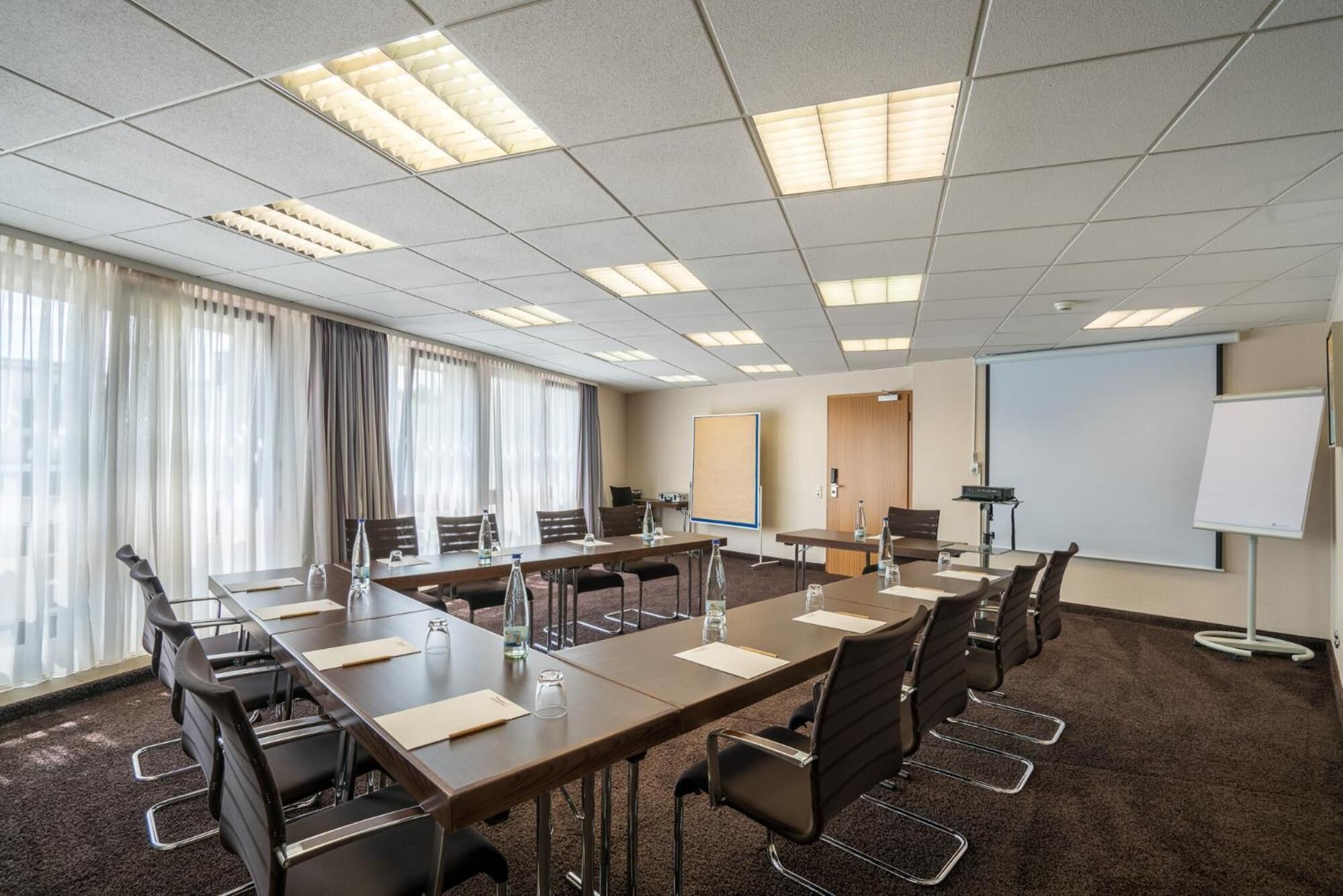 A conference room with a long table, chairs, a whiteboard, and a projector screen.