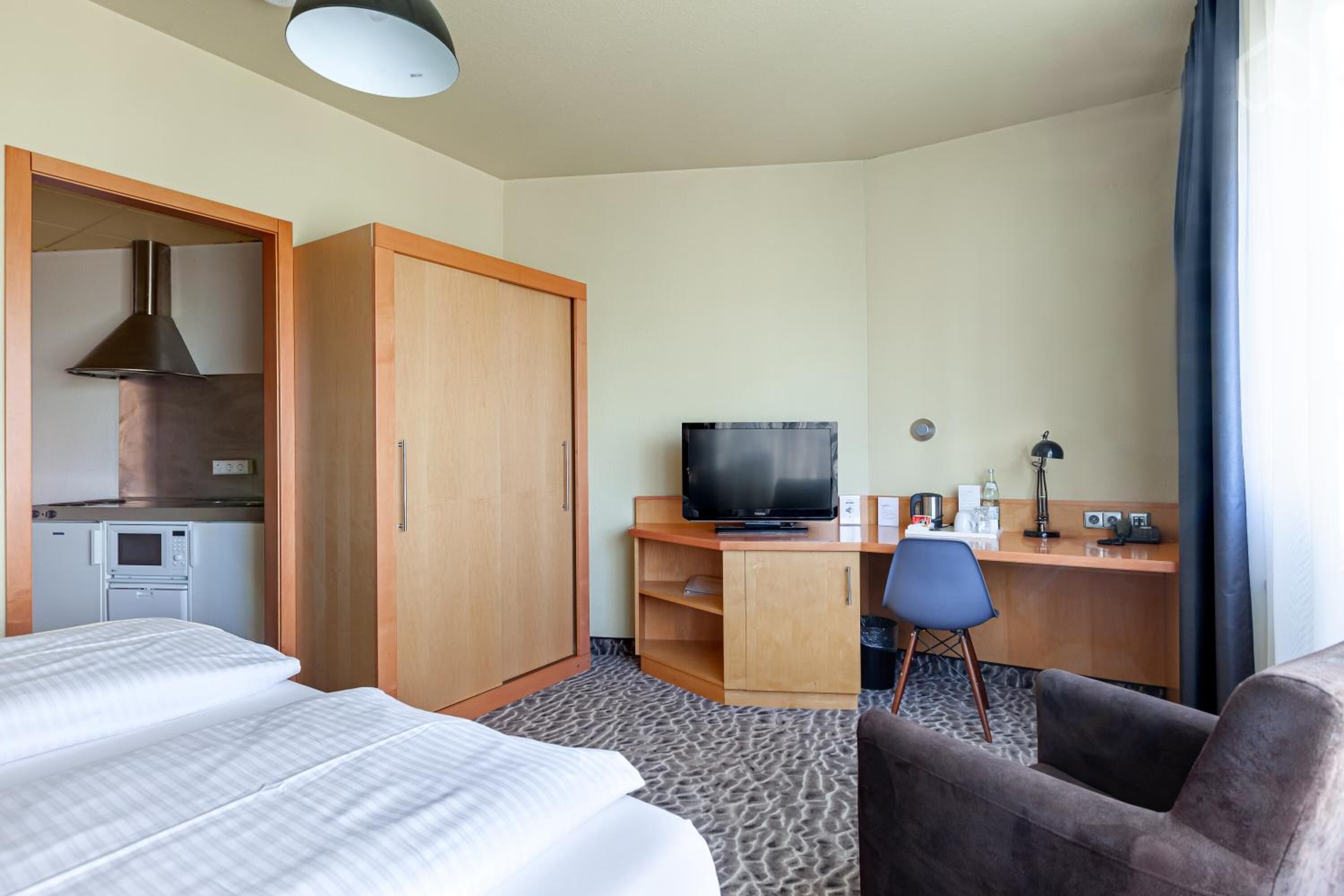 Een hotelkamer met twee bedden, een bureau met een televisie, een kitchenette en een stoel.