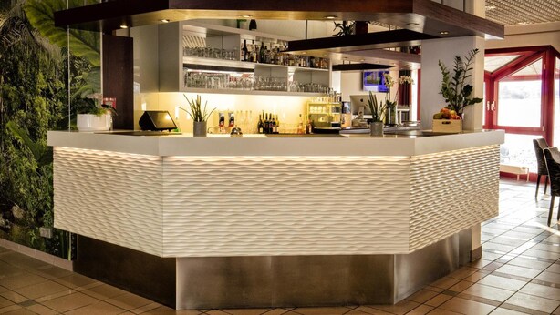 Un espace bar moderne avec un comptoir à surface texturée, des étagères remplies de bouteilles et des plantes en pot.
