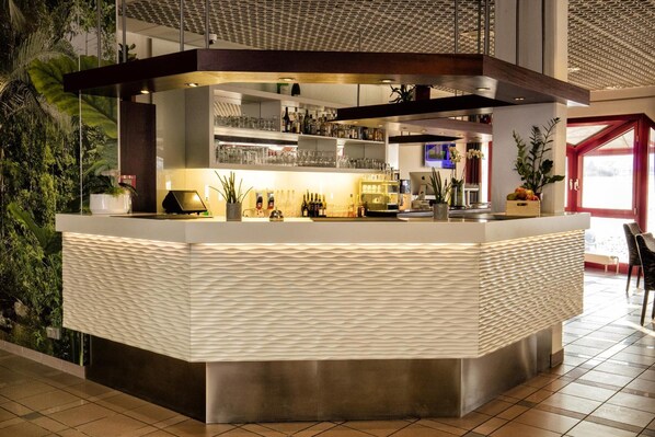 A modern bar area with a textured countertop, shelves with bottles, and potted plants. - LOFTSTYLE Hotel Gerlingen, Sure Hotel Collection by B/W (Gerlingen)