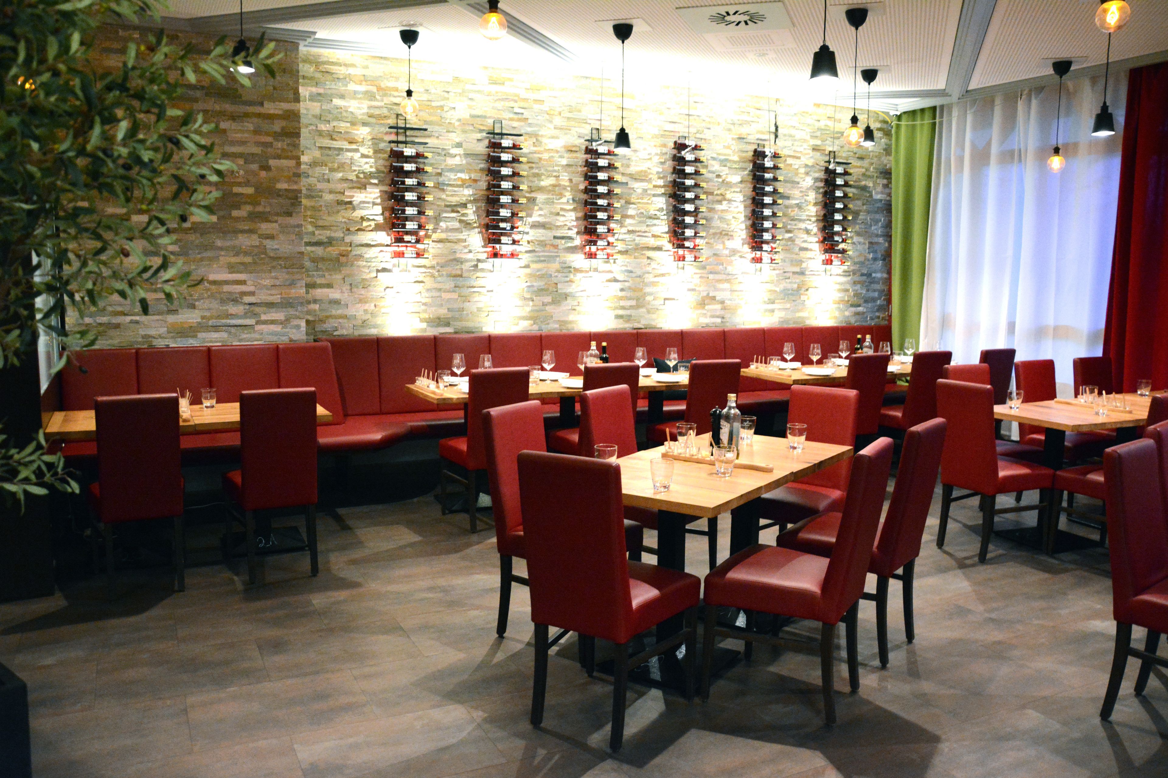 A restaurant with red booths and tables, a stone wall, and hanging light fixtures.