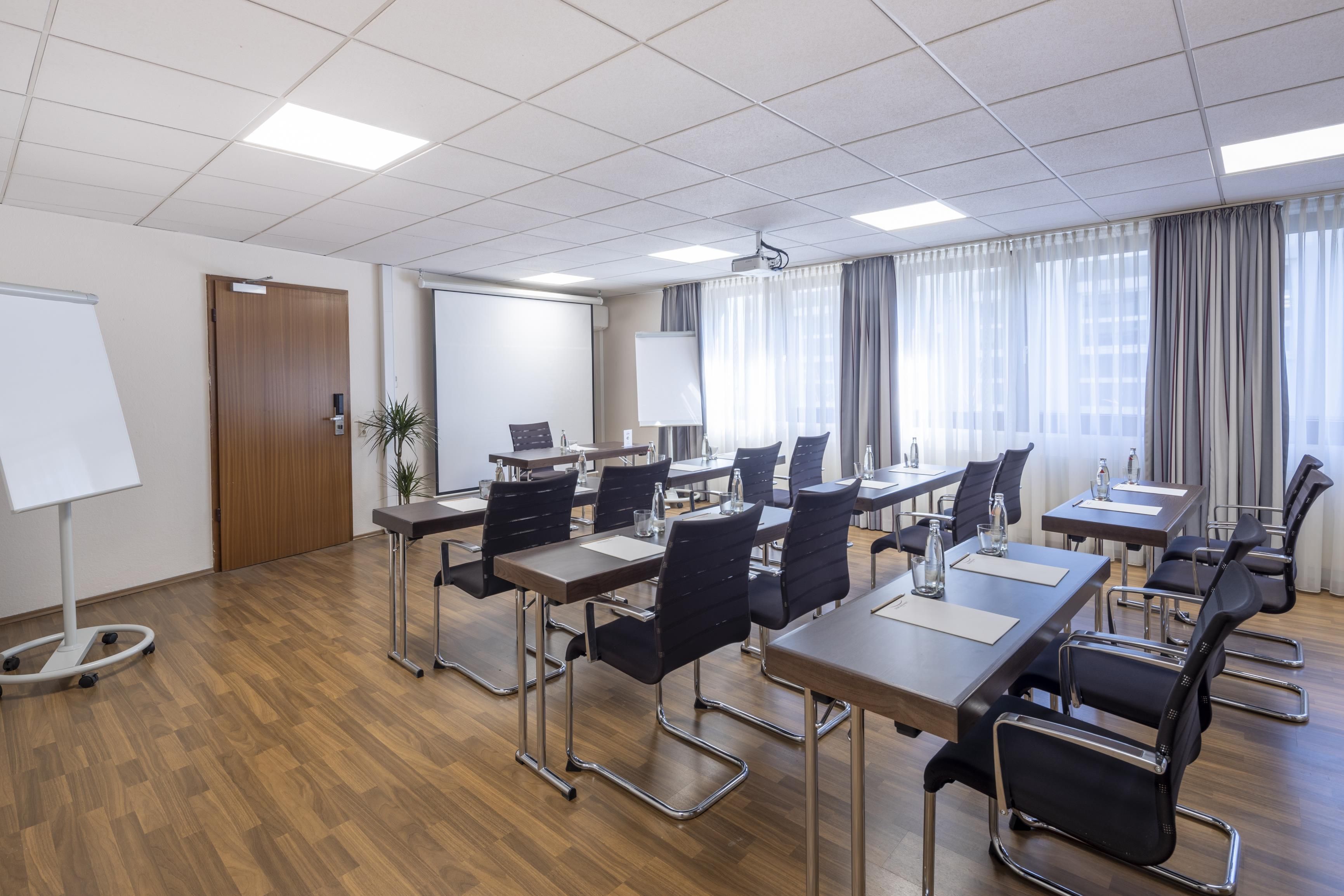 Un salón de conferencias con varias mesas y sillas, una pizarra y una pantalla de proyector.