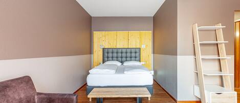 Un dormitorio con una cama, un banco de madera, un sofá marrón y una escalera de madera apoyada en la pared.