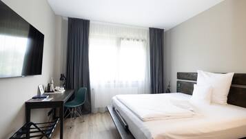 A hotel room with a bed, a desk, a chair, a TV, and a window with curtains.