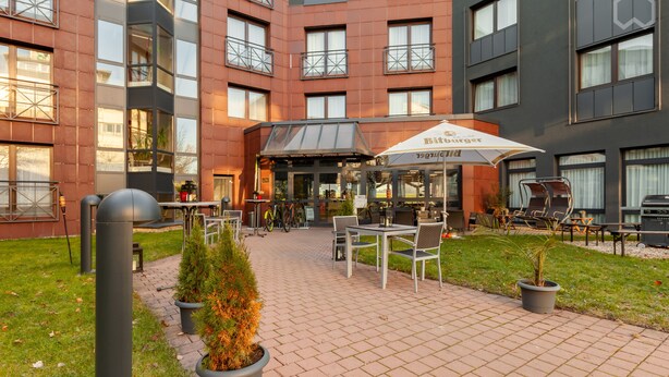 A hotel courtyard with outdoor seating, potted plants, and a visible entrance to the building. - LOFTSTYLE Hotel Gerlingen, Sure Hotel Collection by B/W (Gerlingen)