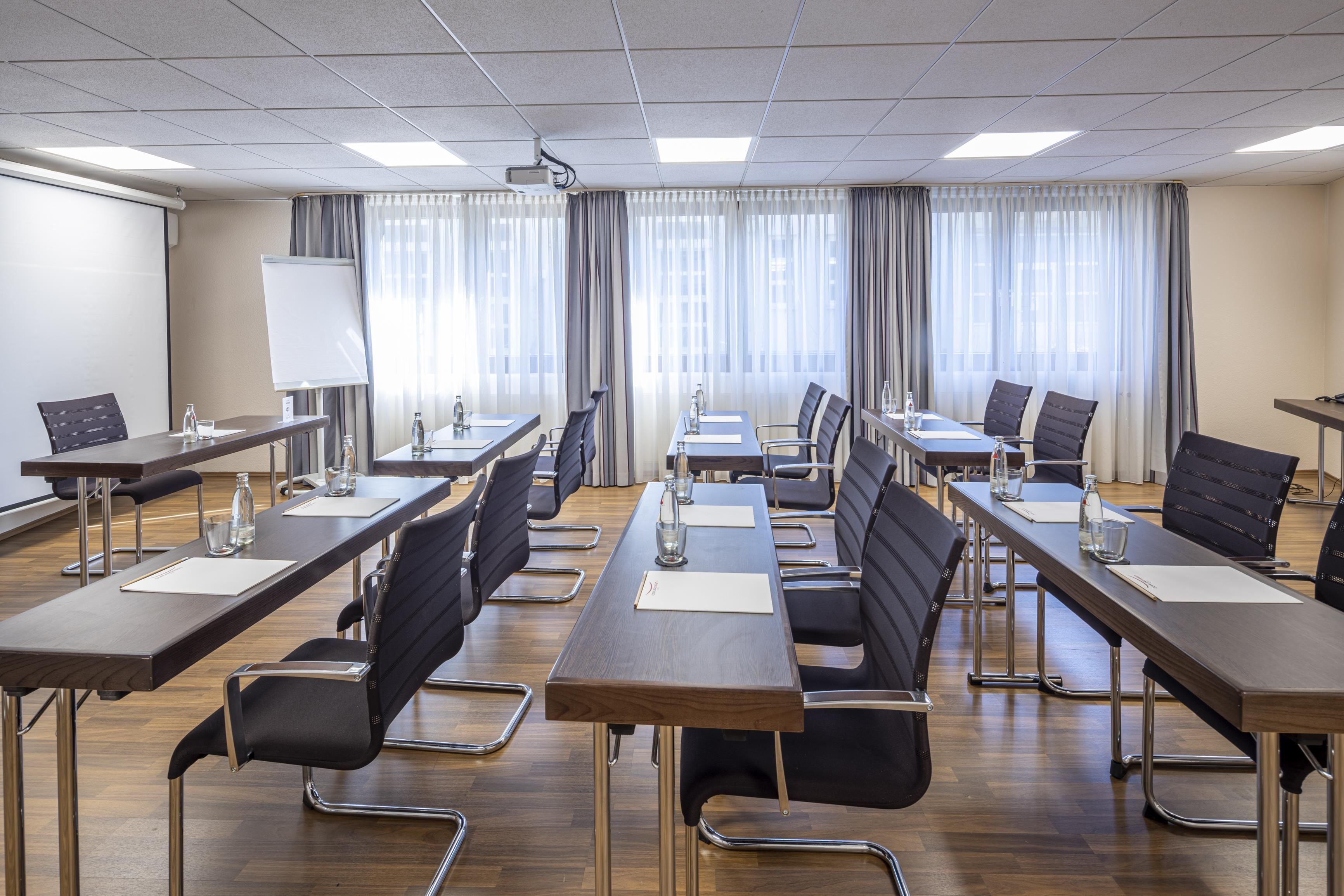 Une salle de conférence équipée de plusieurs tables et chaises, d’un projecteur et d’un tableau blanc.