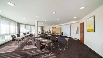 A conference room with multiple tables and chairs, a large screen, and a projector.