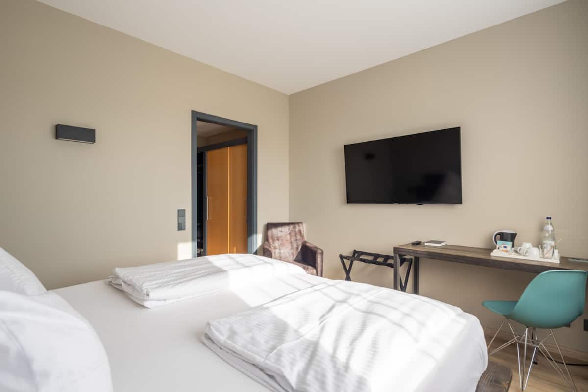 A hotel room with two beds, a desk, a chair, a television, and a door leading to another room.