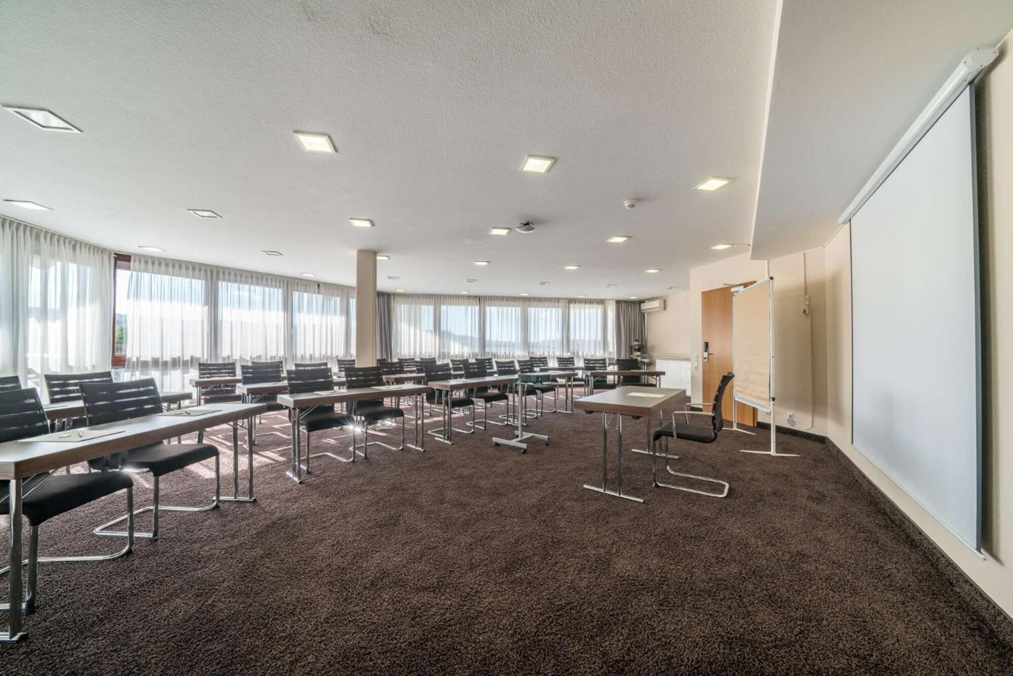 A conference room with multiple tables and chairs, large windows with curtains, and a whiteboard.