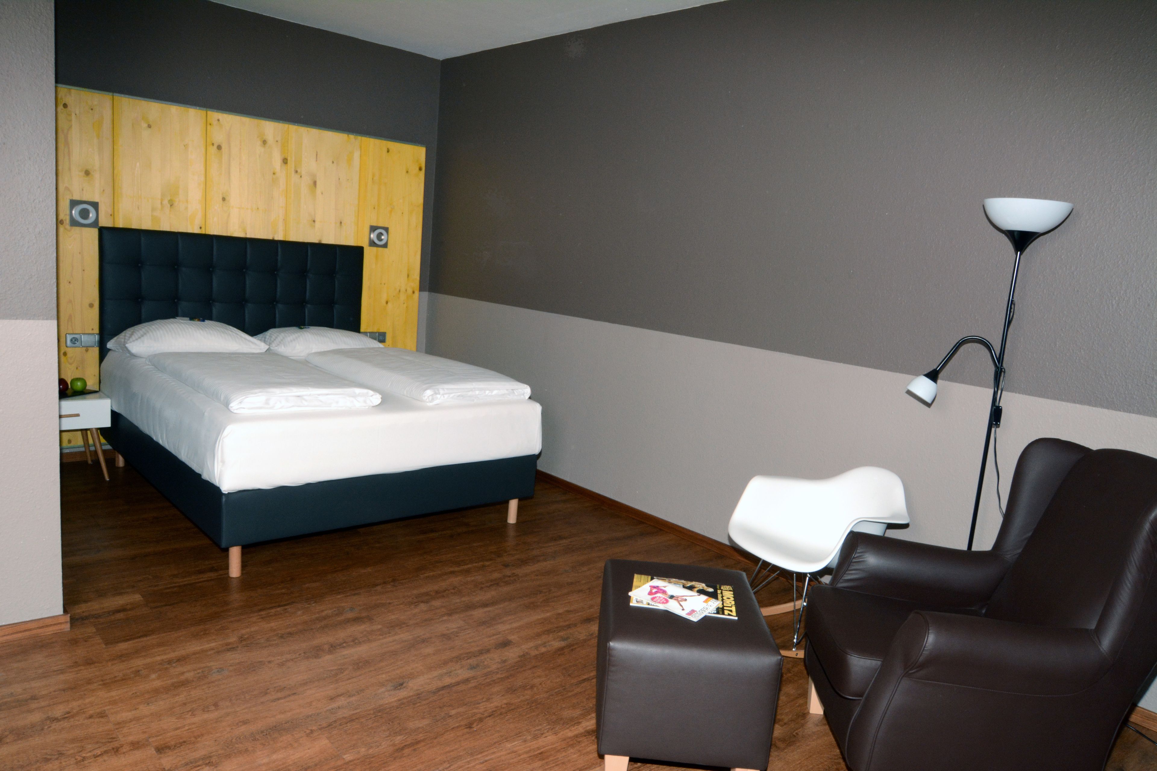 A hotel room with a bed, a desk, a chair, and a floor lamp.