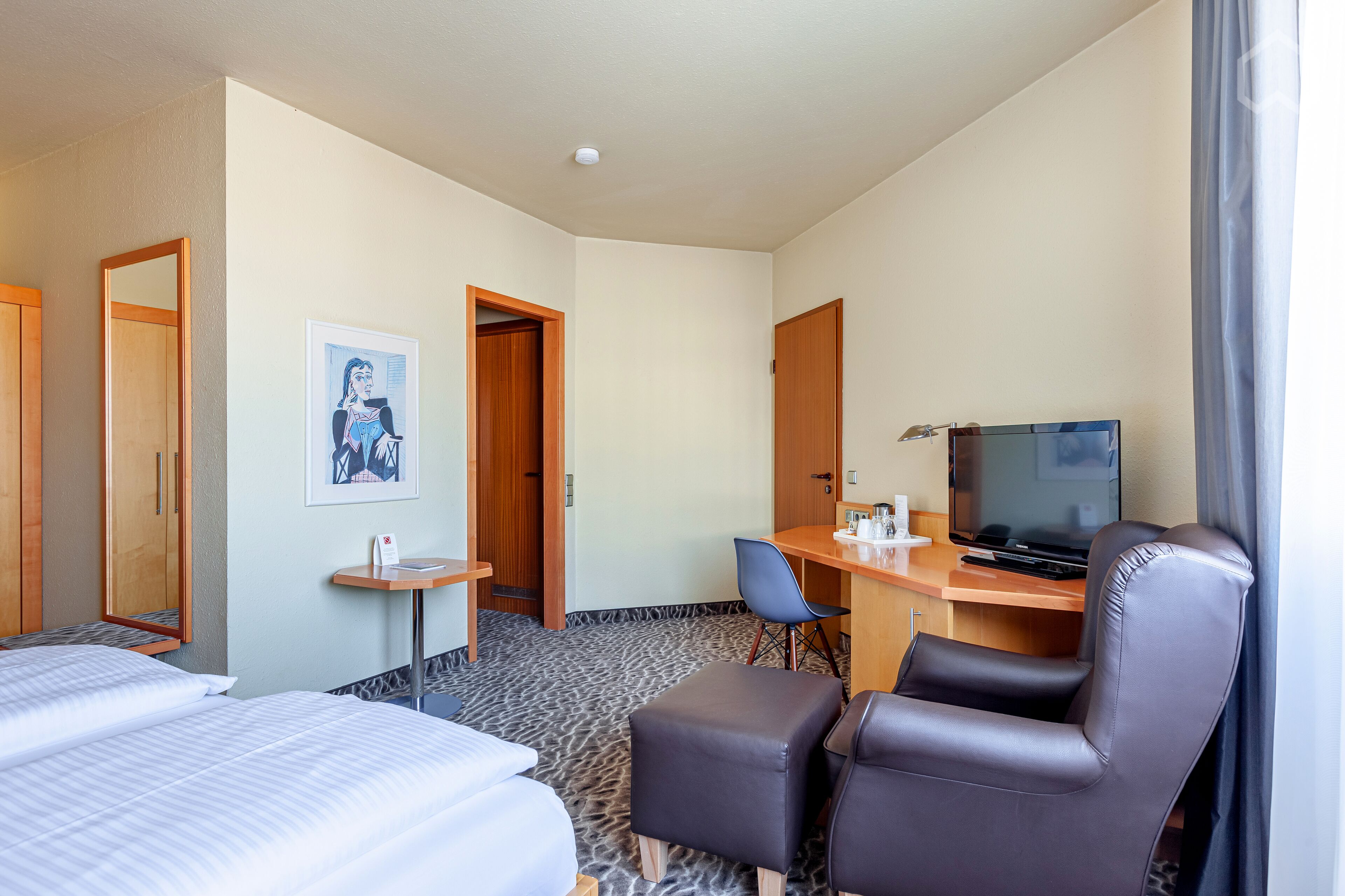 Une chambre d’hôtel comprenant un lit, un bureau avec une chaise, une télévision et une petite table.