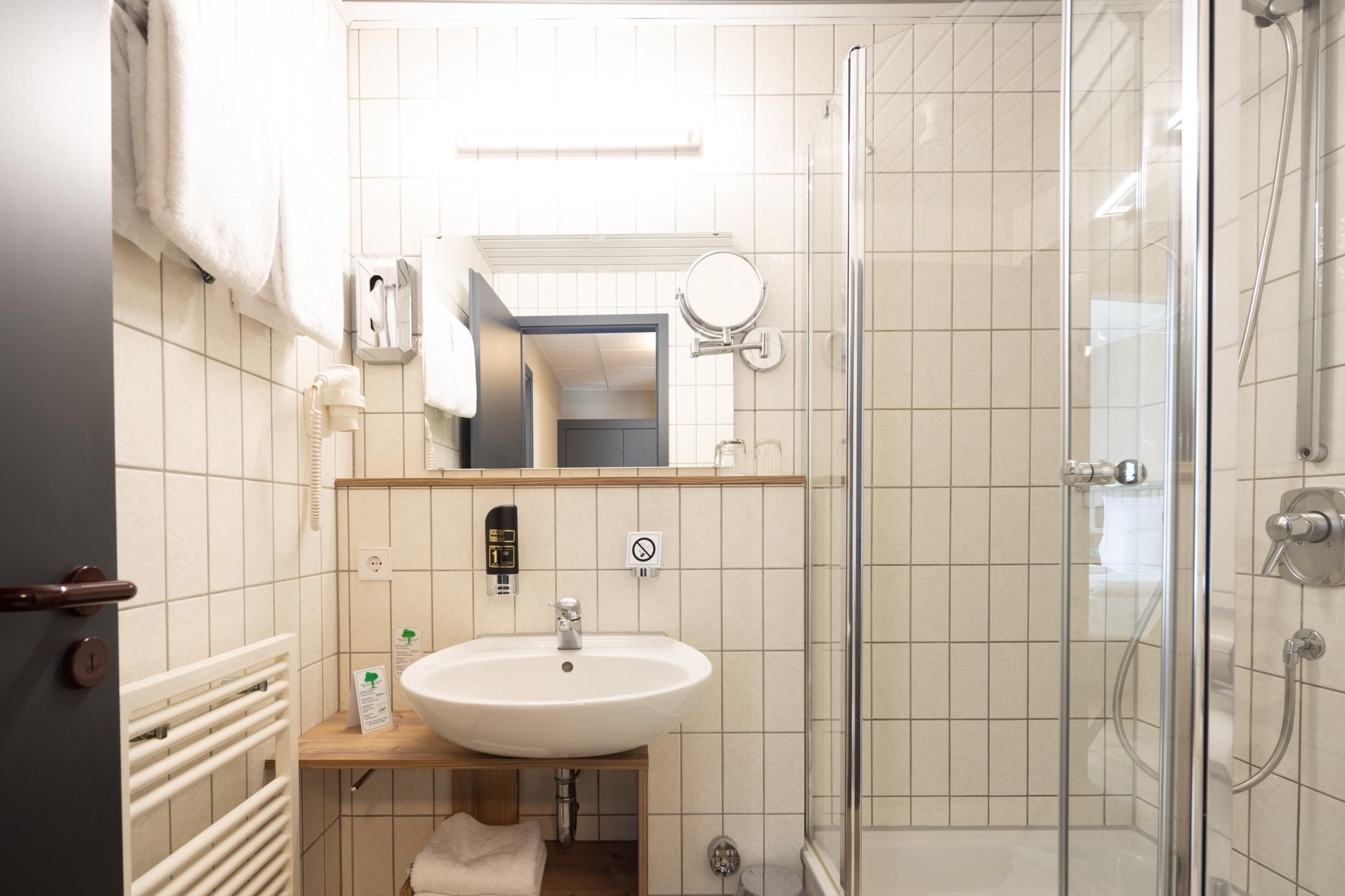 Un baño moderno con cabina de ducha de vidrio, un lavamanos blanco y un espejo encima.