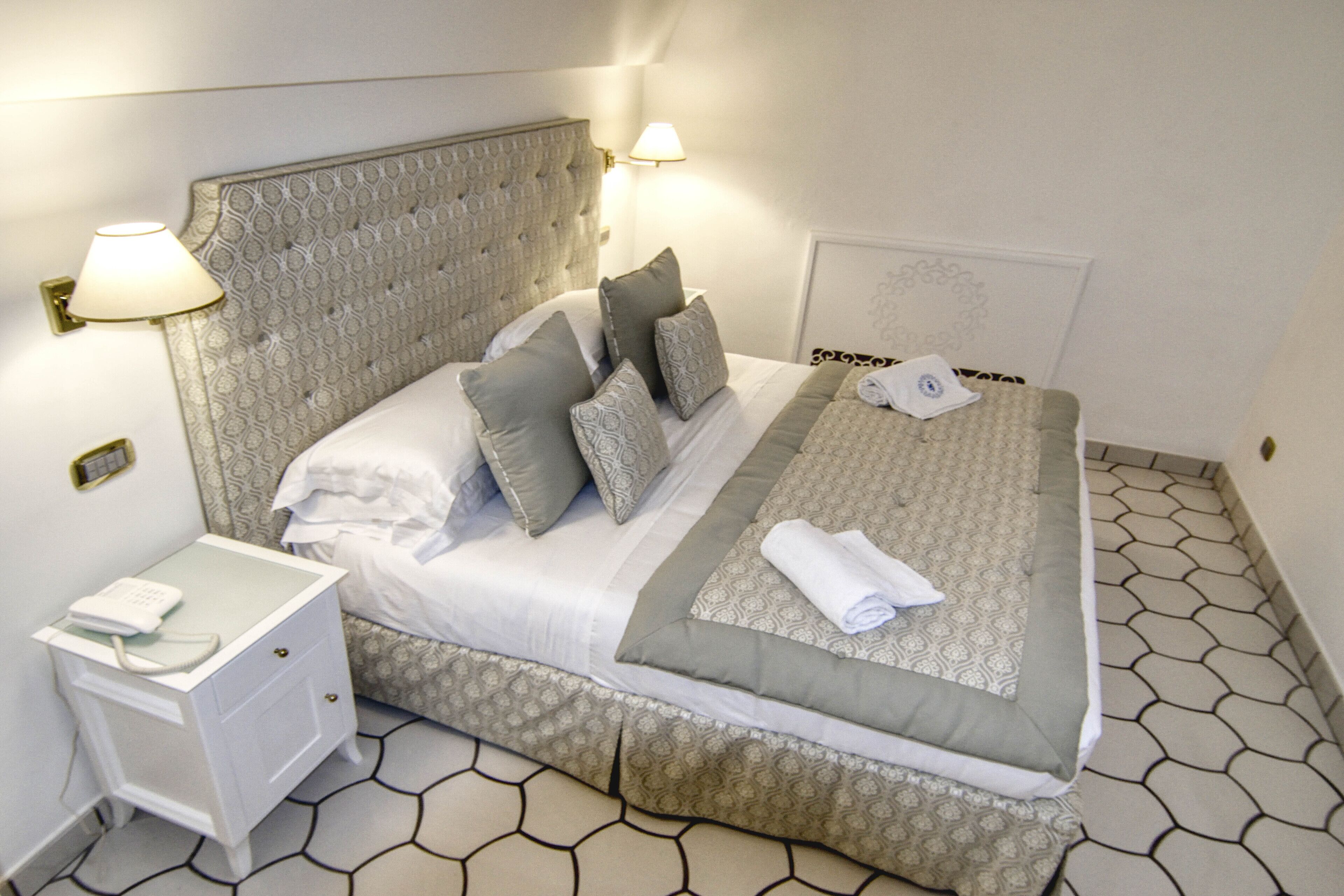 Una cama bien hecha con ropa de cama y almohadas estampadas, una mesita de noche con lámpara y teléfono.