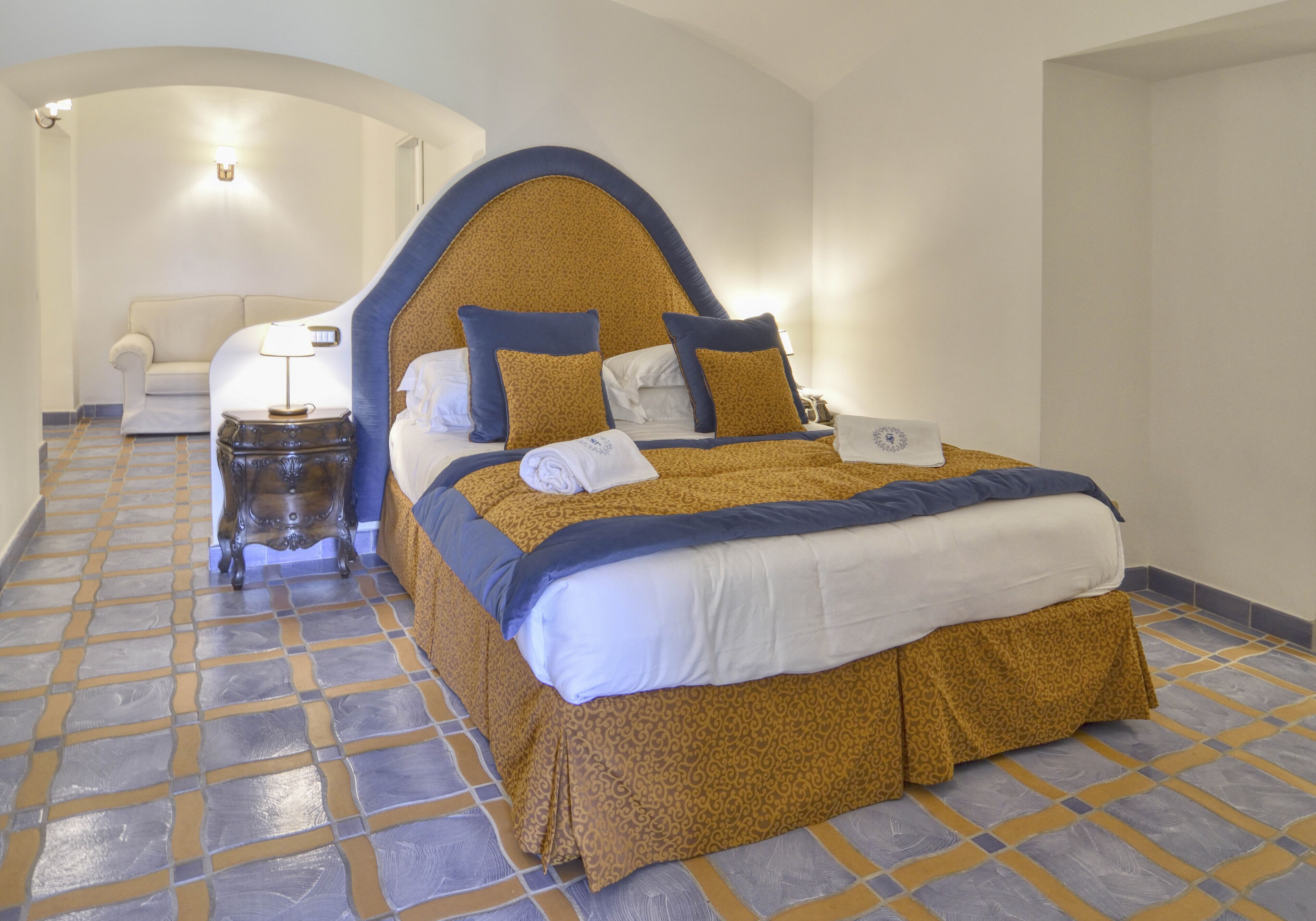 A hotel room with a large bed, a nightstand, a lamp, and a sofa.