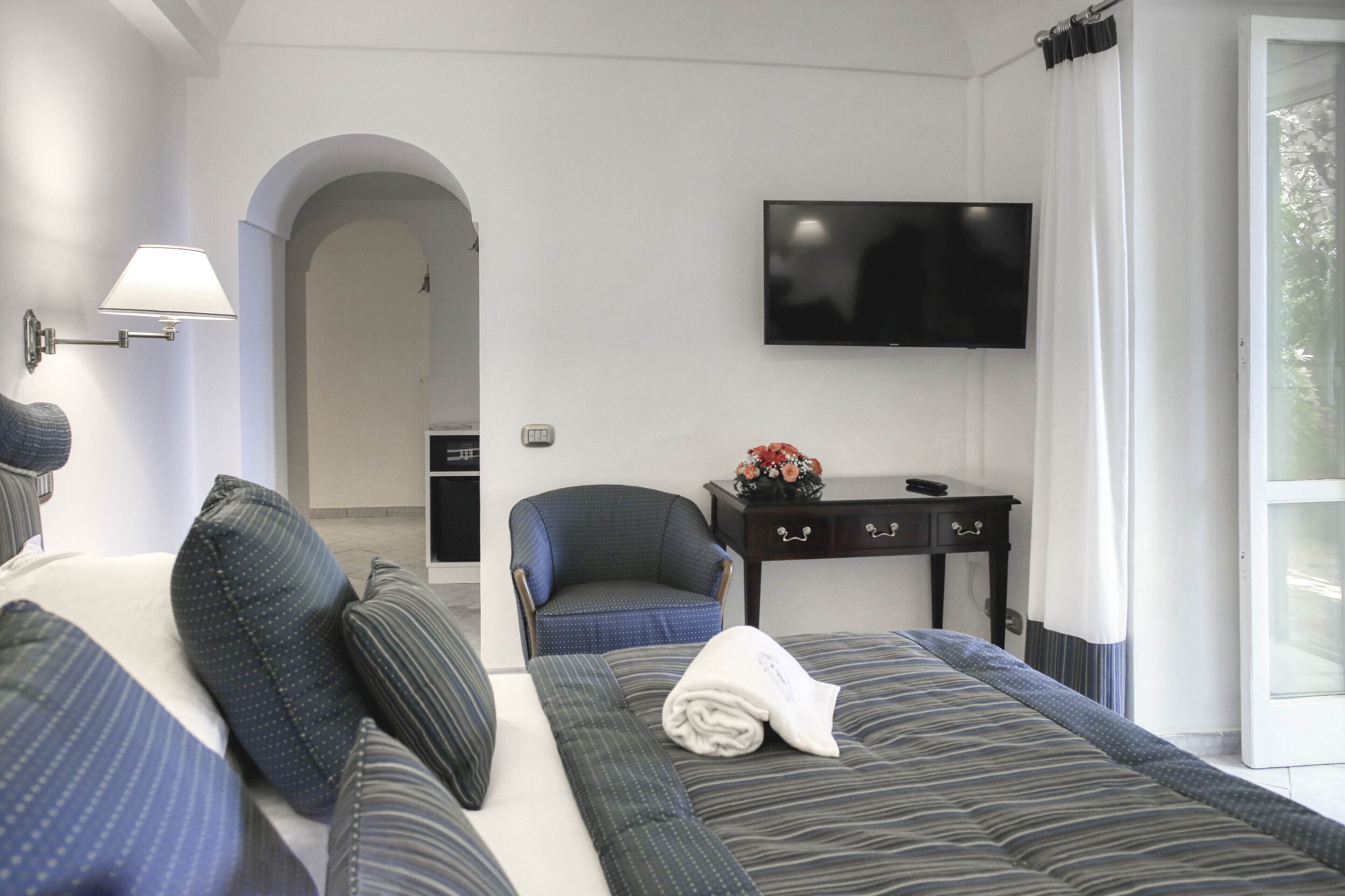 Une chambre d’hôtel avec un lit, une chaise, une télévision et un bureau agrémenté d’un vase de fleurs.