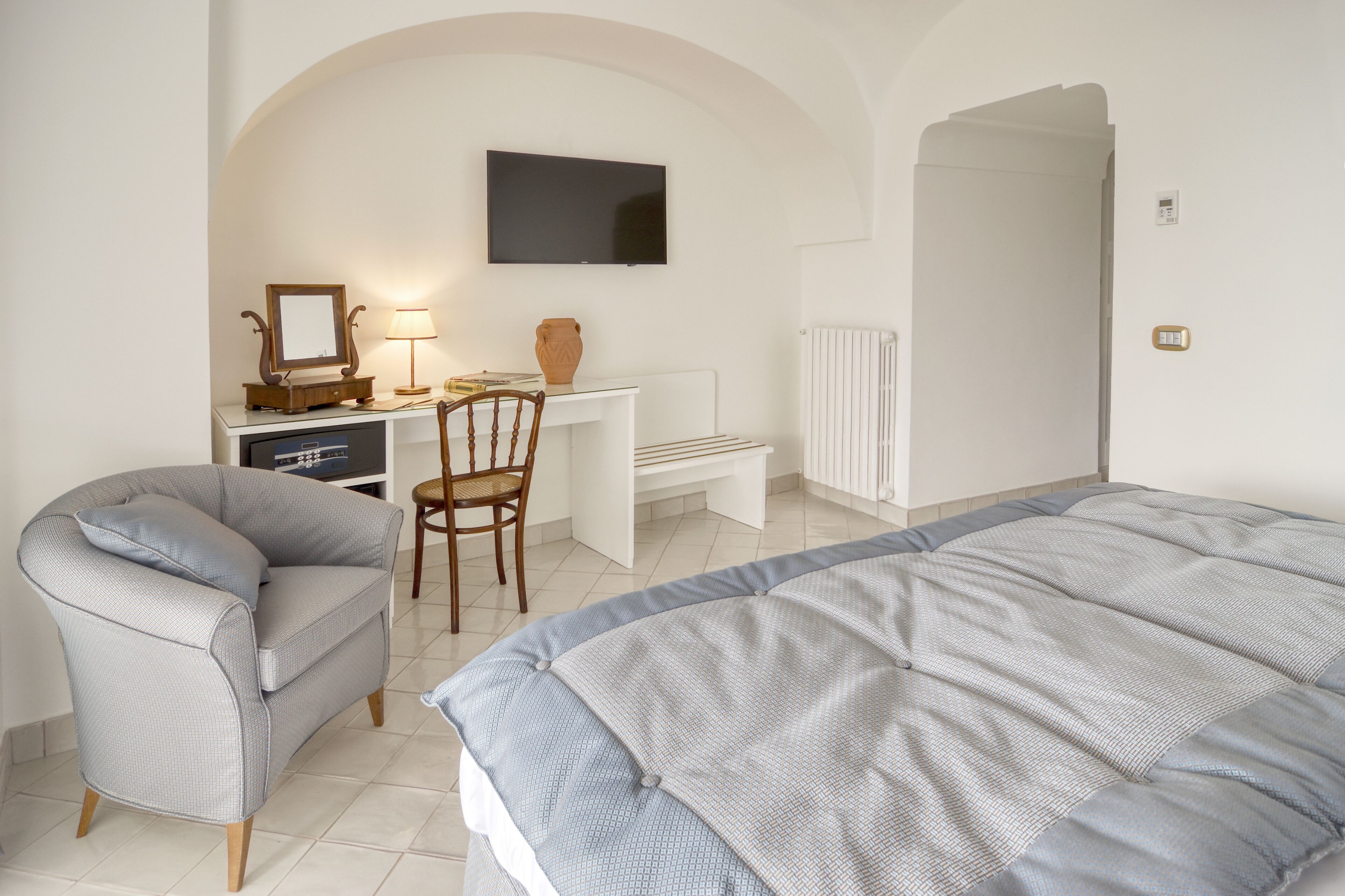 Una camera da letto con un letto, una sedia, una scrivania, una televisione e un termosifone.