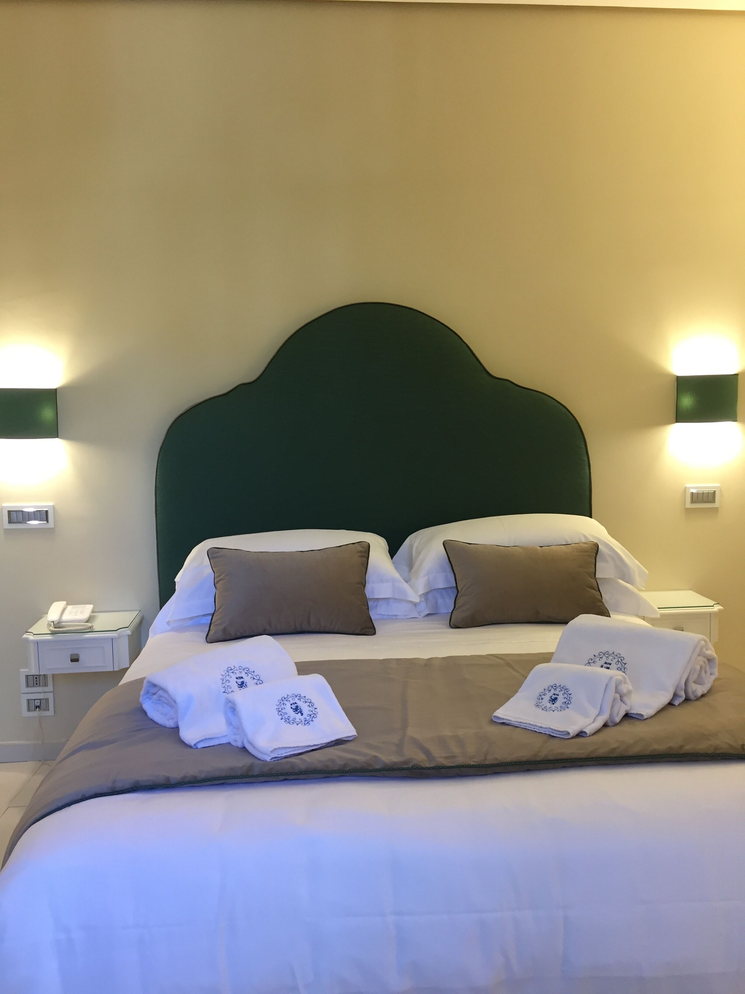 A hotel room with a large bed, two bedside tables, and wall-mounted lights.