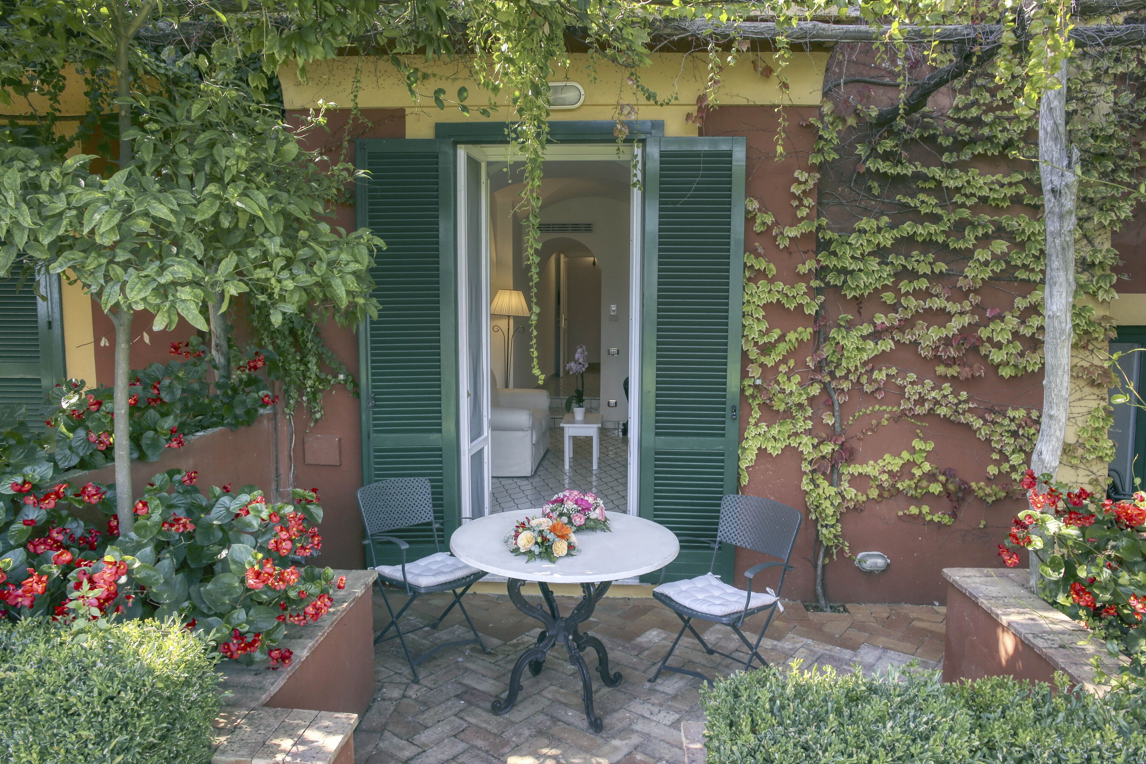 Une terrasse extérieure avec une table ronde, deux chaises et un vase de fleurs.