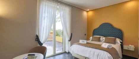 A hotel room with a bed, a table with a chair, and a view of the outdoors through a sliding door.