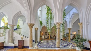 A spacious interior with high arched ceilings, a central staircase, and hanging plants. - Palazzo Confalone (Ravello)